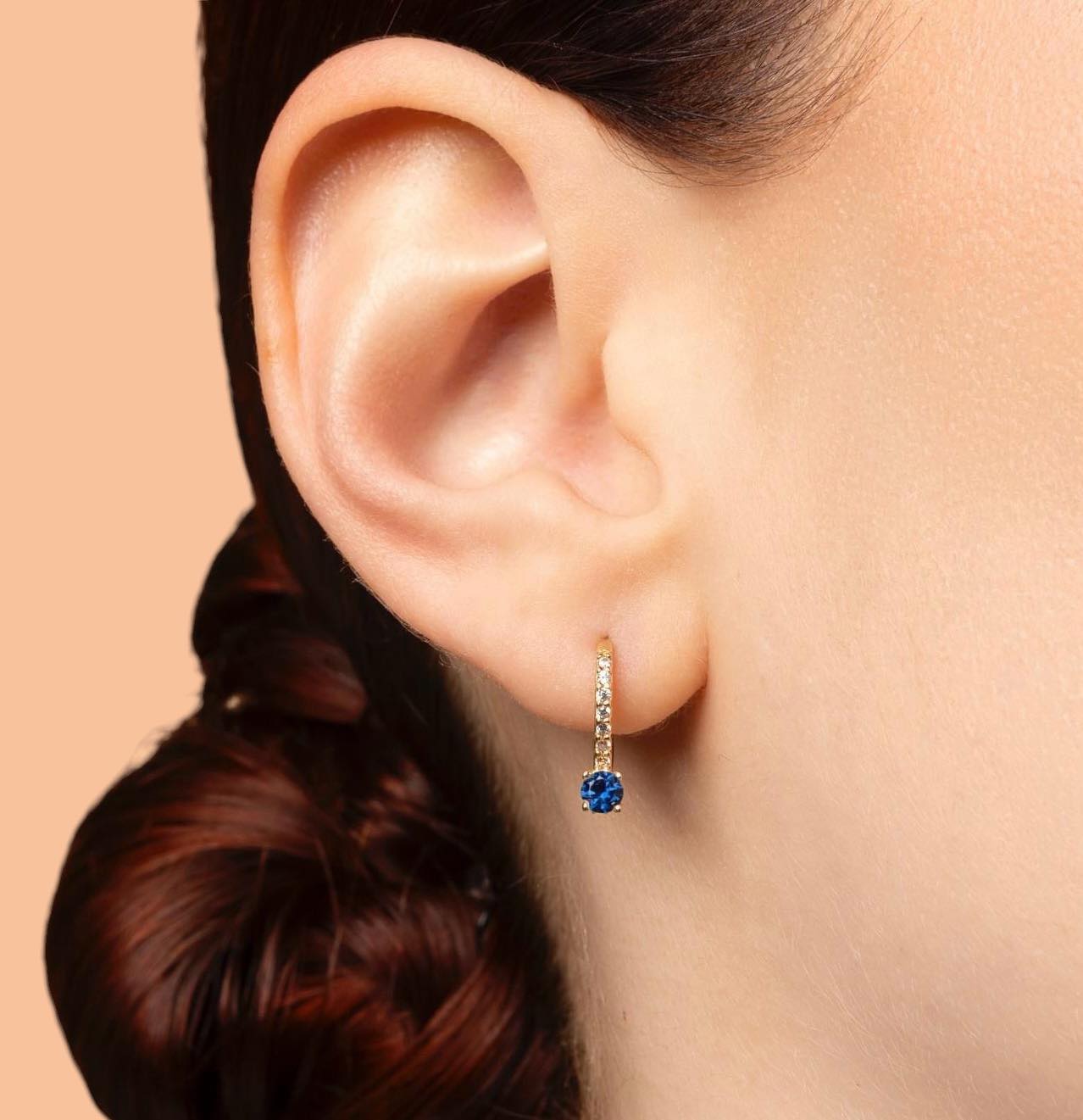 Elegant 14K gold children's earrings featuring a dangling blue sapphire and small cubic zirconia stones, designed to be worn on the ear. The earrings feature a secure English clasp and are suitable for older girls.