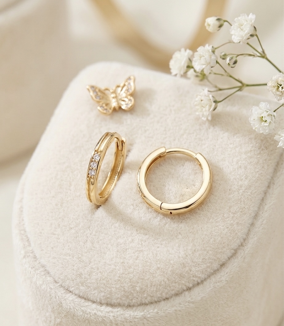 A close-up of a pair of small, smooth 14-karat gold rings from Asto Gold, set in a delicate velvet box. The rings are rounded, with no sharp edges, and feature a subtle sparkle from zirconia stones, making them ideal for children to wear every day. 